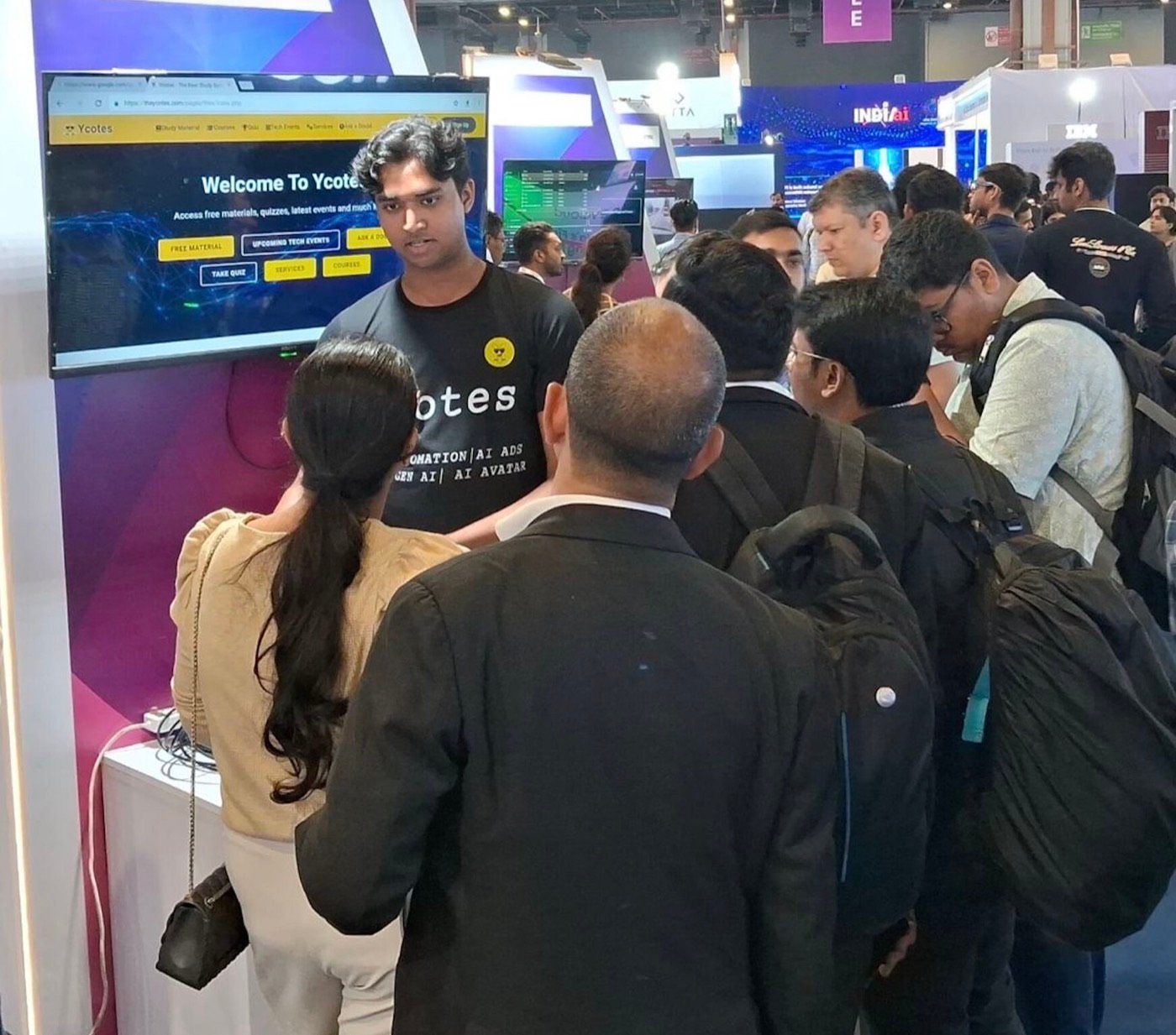 Chirag Jain presenting Ycotes to a crowd at the Ycotes stand during the International AI Summit, with the INDIAai and IBM stands behind